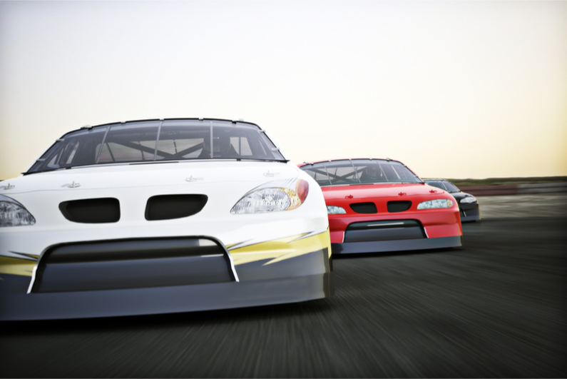 Front view of auto racing race cars racing on a track with motion blur.