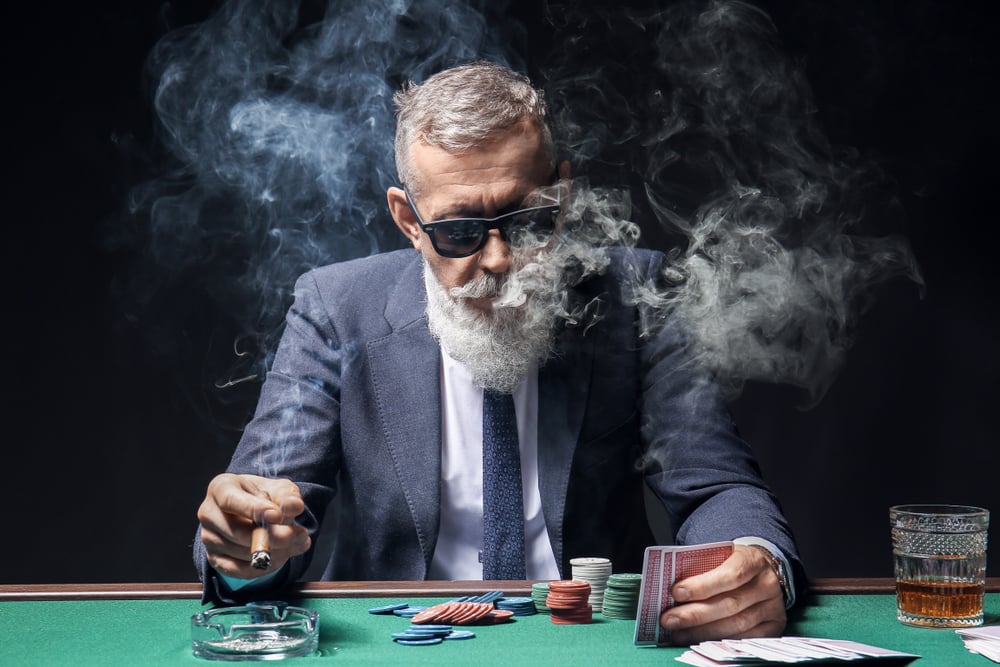 man in suit smoking cigar while at a gambling table