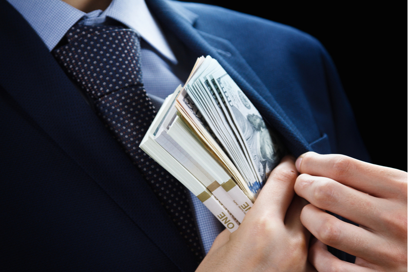 male in suit hiding wads of dollar bills in his jacket