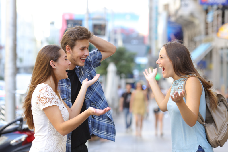 Two friends happily greeting a third on a city street